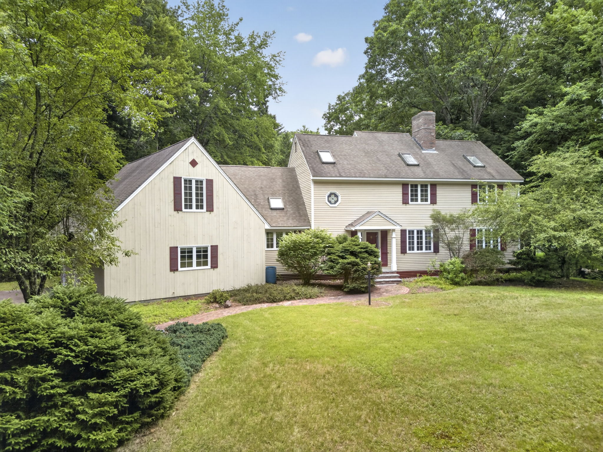 Cream New England colonial home with maroon shutters on a green summer lawn in Bedford NH