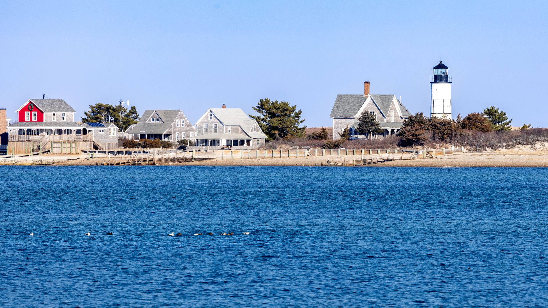 New England coastal village of shingle-style homes and a white lighthouse seen across open blue water, the kind of Seacoast setting that draws homebuyers to Portsmouth, NH