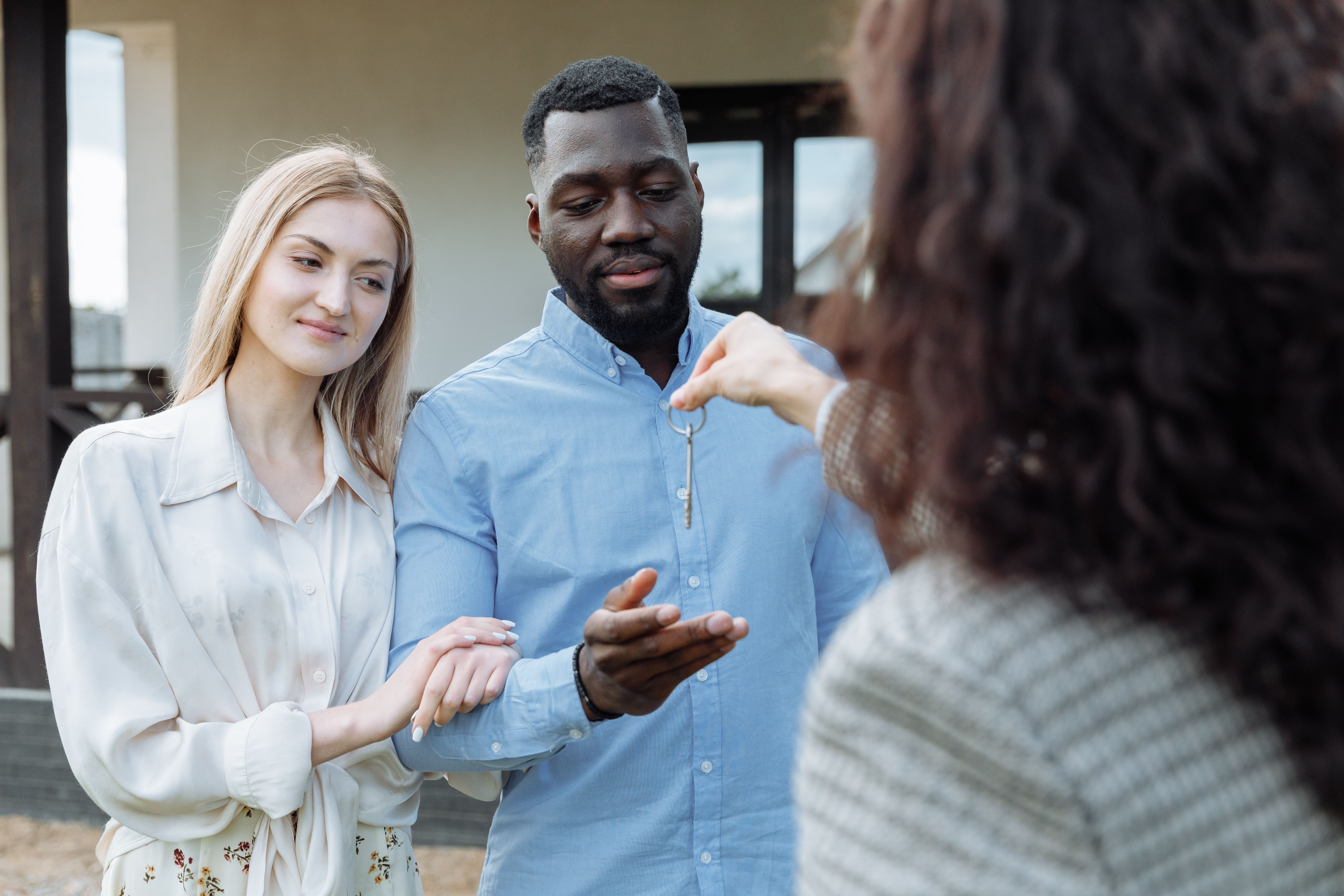 Real estate agent handing house keys to a happy couple outside their new home after winning a New Hampshire offer