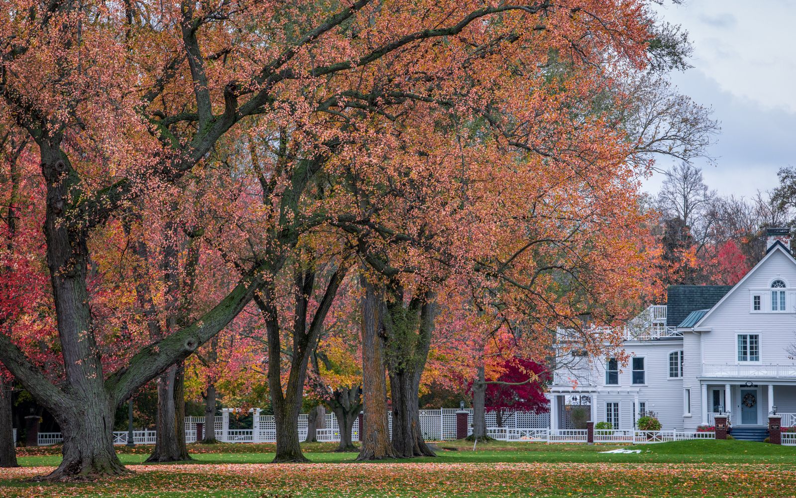 White New England clapboard house behind a picket fence under peak fall foliage - NH towns for first-time home buyers