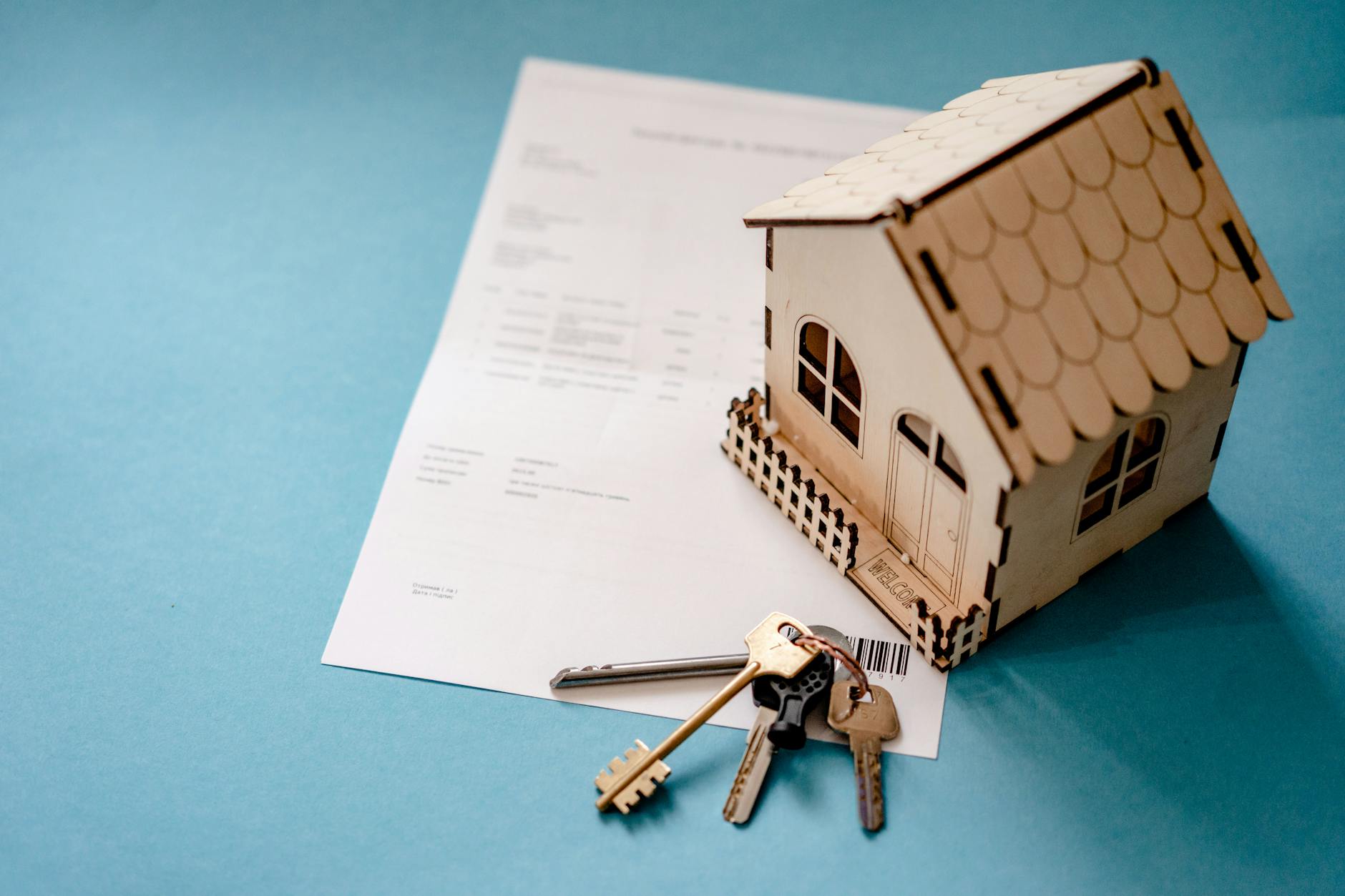 Wooden model home with keys resting on a purchase contract, symbolizing planning a New Hampshire home purchase and septic inspection