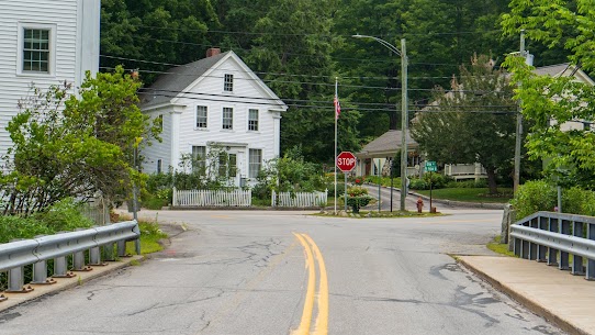 Charming residential street with a classic white clapboard colonial home in a small New England town — the kind of family-friendly setting found in the best towns in New Hampshire for families