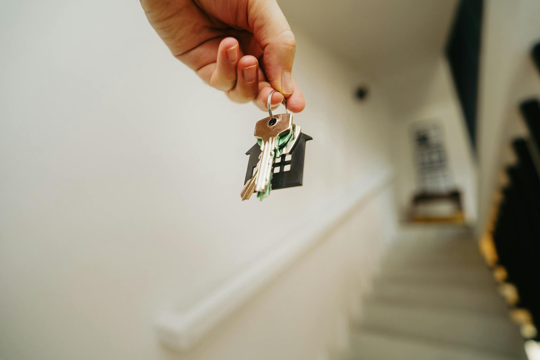 Hand holding house keys on a home-shaped keychain in a bright New England entryway, symbolizing the payoff of hiring the right NH real estate agent