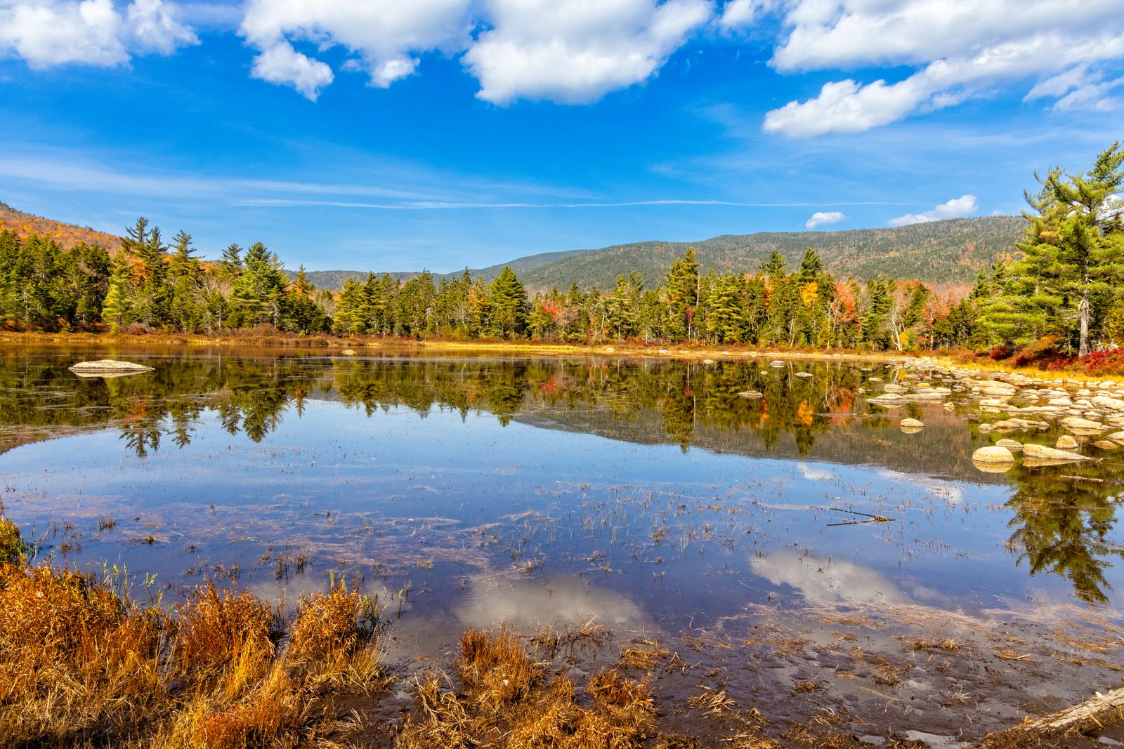 Calm mountain pond ringed by early-fall foliage and evergreens in northern New England - the lake and mountain towns where New Hampshire property tax rates run lowest