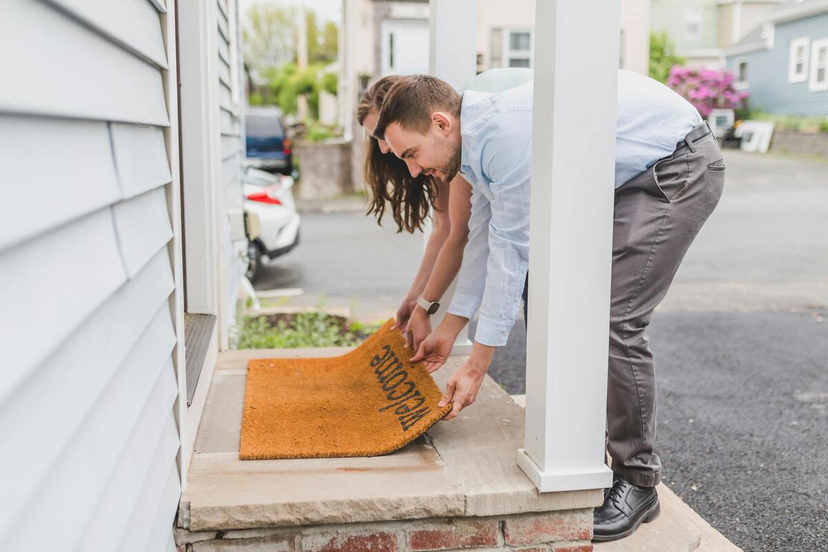 Couple laying down welcome mat in front of home.