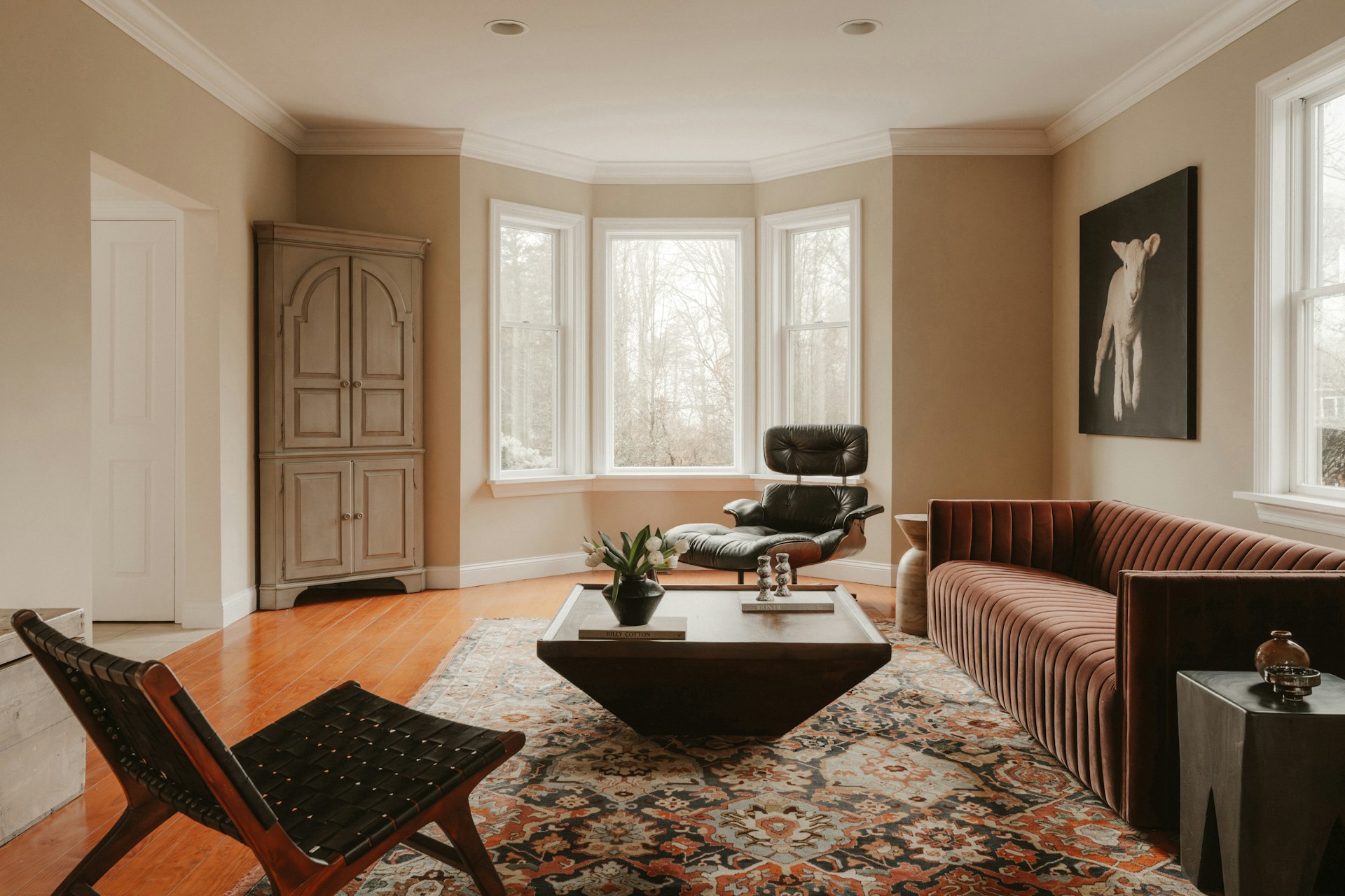Modern living room with a channel-tufted velvet sofa, black lounge chair, bay window light, and patterned rug in a quiet-luxury interior