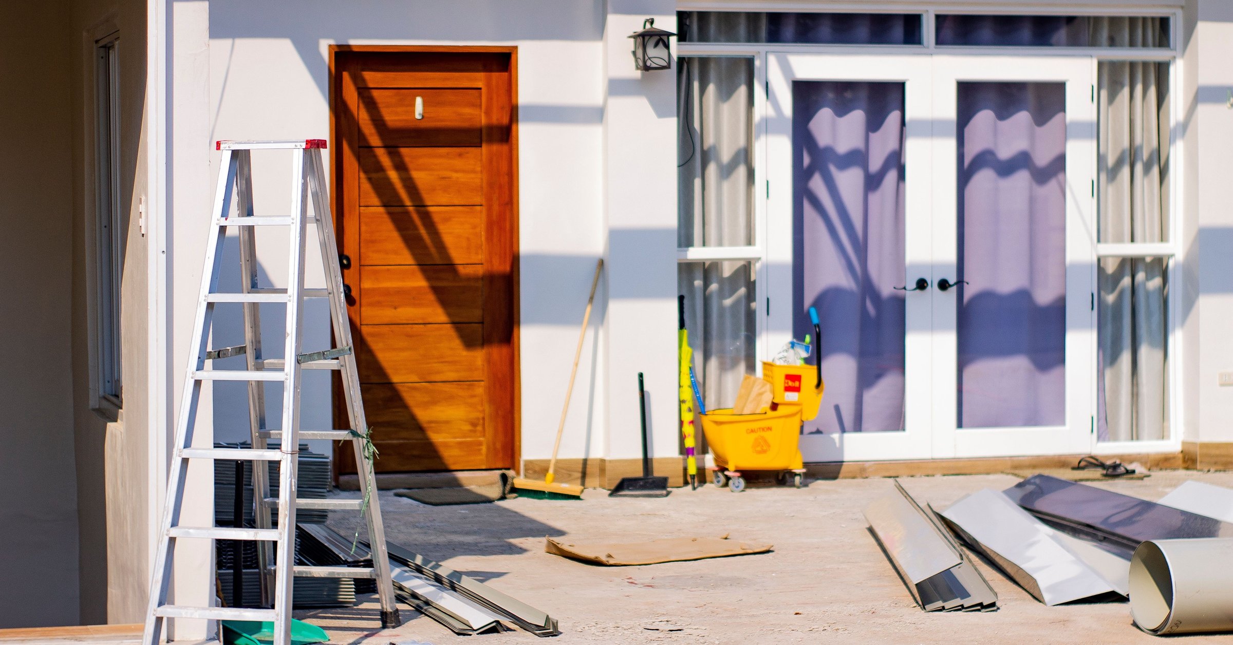 Home exterior mid-renovation with ladder and tools, representing repair decisions before selling a house