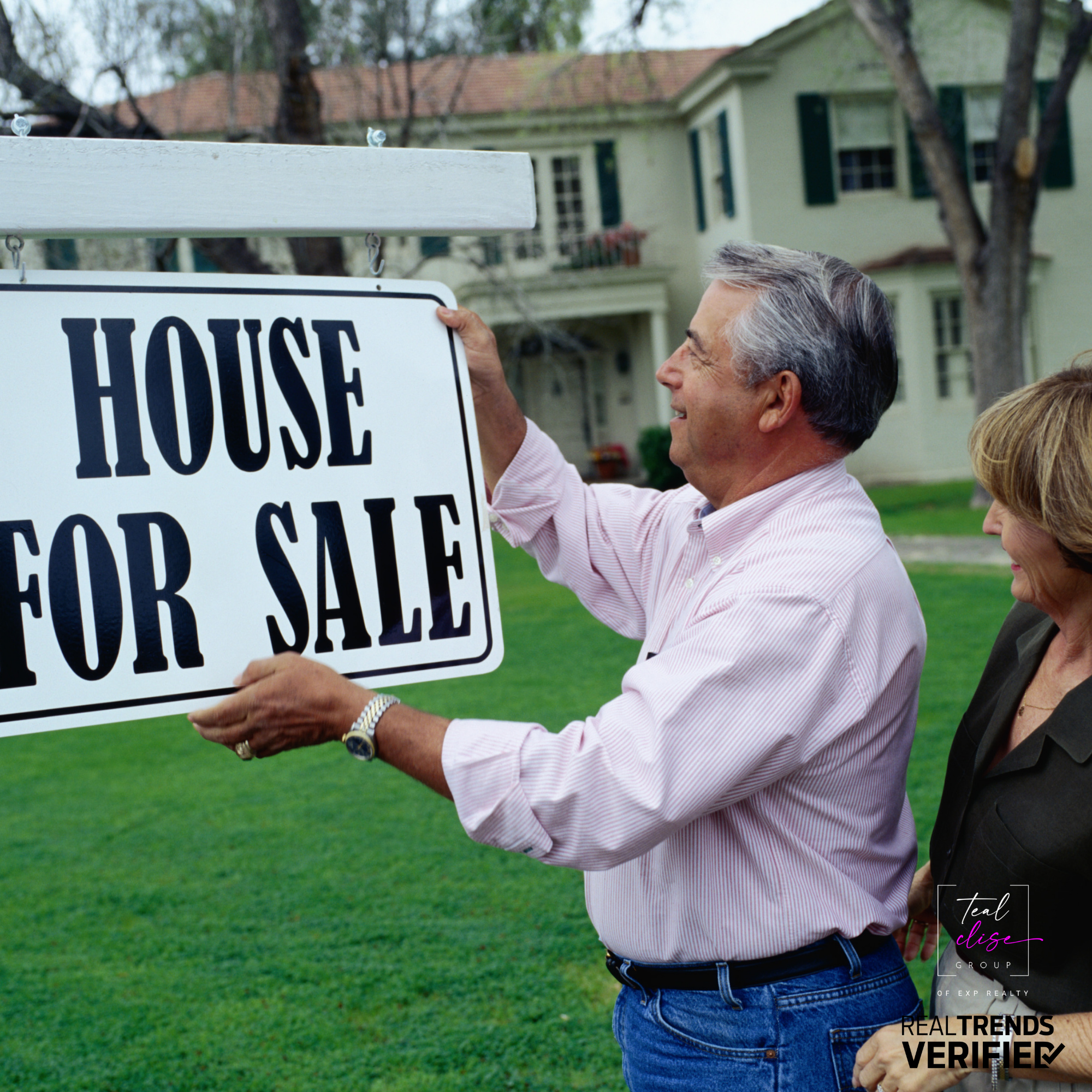 Older couple placing a “House For Sale” sign in front of a Maryland home, symbolizing the right time to sell with the Teal Clise Group.