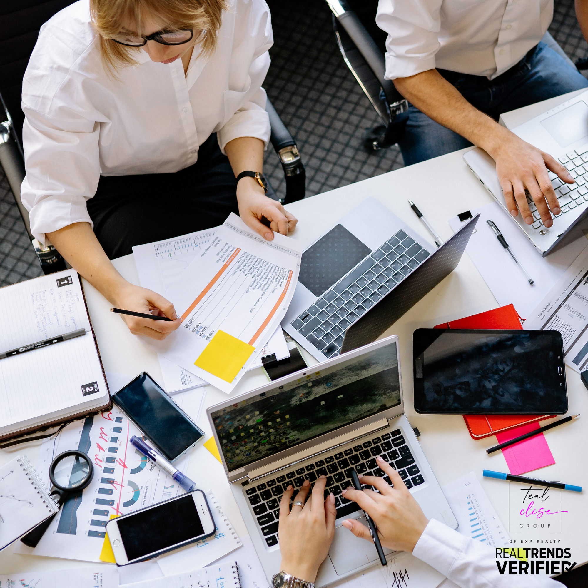 Teal Clise Group admin team collaborating at a desk with laptops, paperwork, and marketing materials, representing the behind-the-scenes support that helps Maryland buyers and sellers succeed.