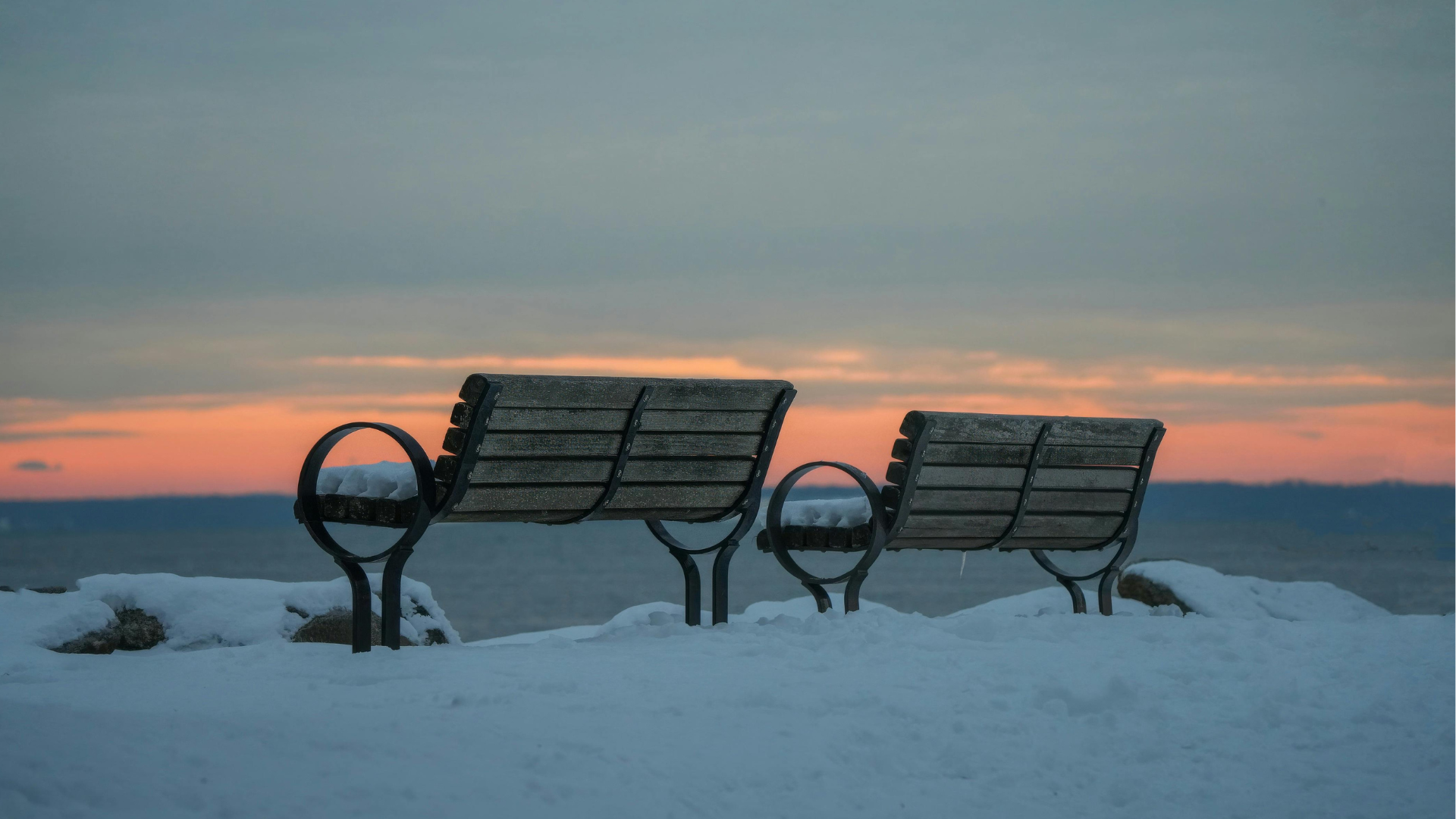 Two benches in the snow overlooking a cloudy sunset on the horizon