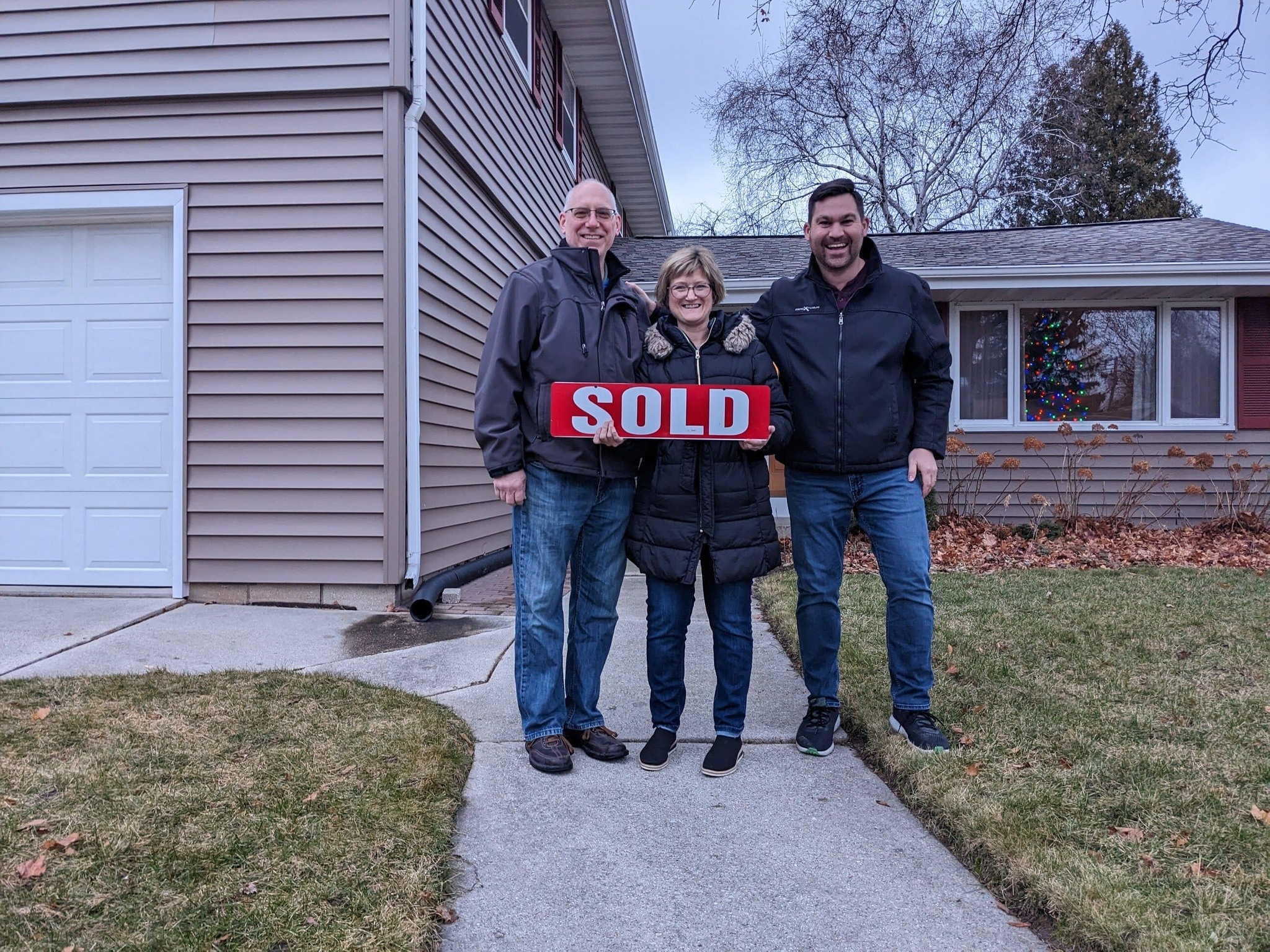 A couple standing with their realtor holding a SOLD sign smiling