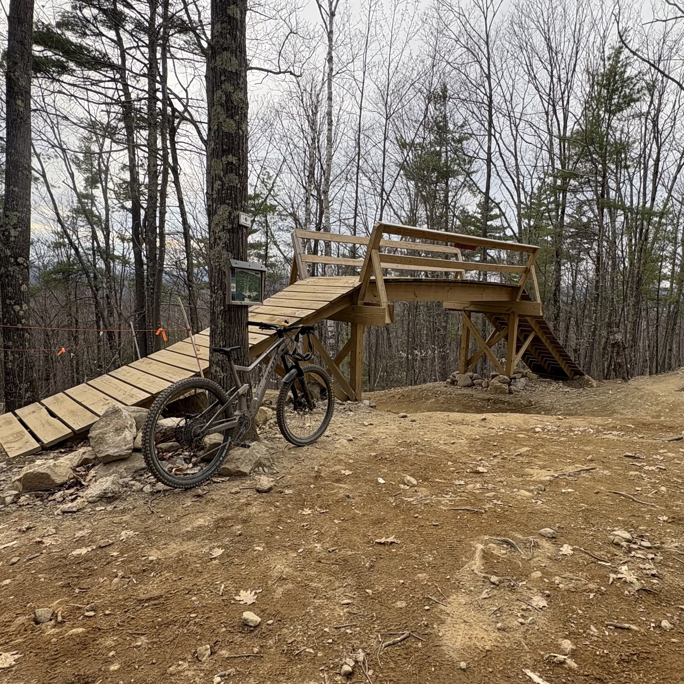 A mountain bike leans against a tree at the base of a wooden bridge feature at Highland Mountain Bike Park