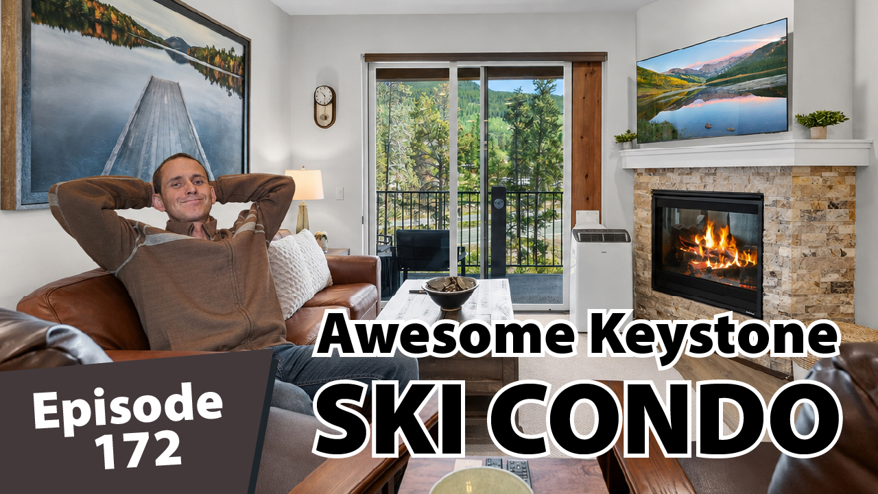 Matt Dayton relaxes with his hands behind his head inside a bright Keystone condo, with mountain views through the balcony doors and a glowing stone fireplace beside him.