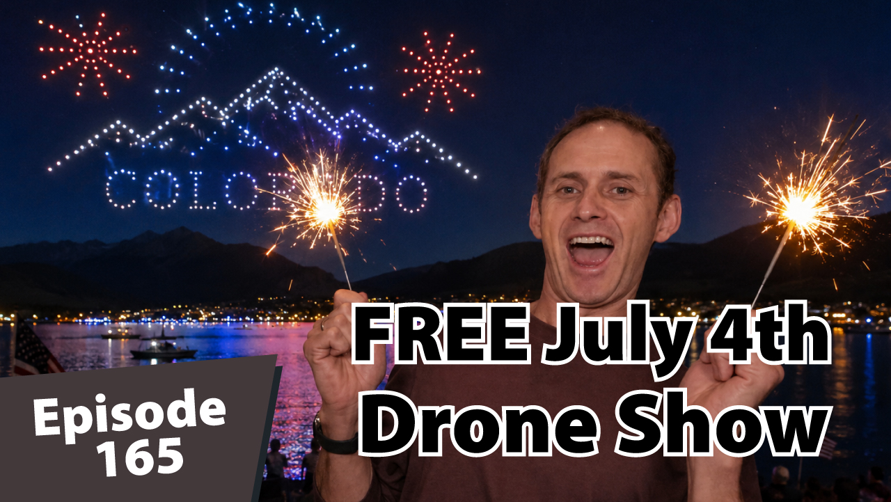 Matt Dayton smiles while holding sparklers in front of a nighttime Lake Dillon celebration with colorful drone lights, mountain silhouettes, and patriotic Fourth of July scenery.