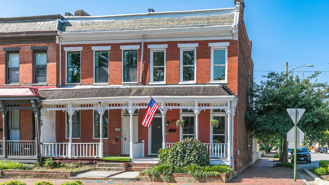 a brick italianate style rowhome sits on the corner of a streeth. The sidewalks along the front and side are brick.