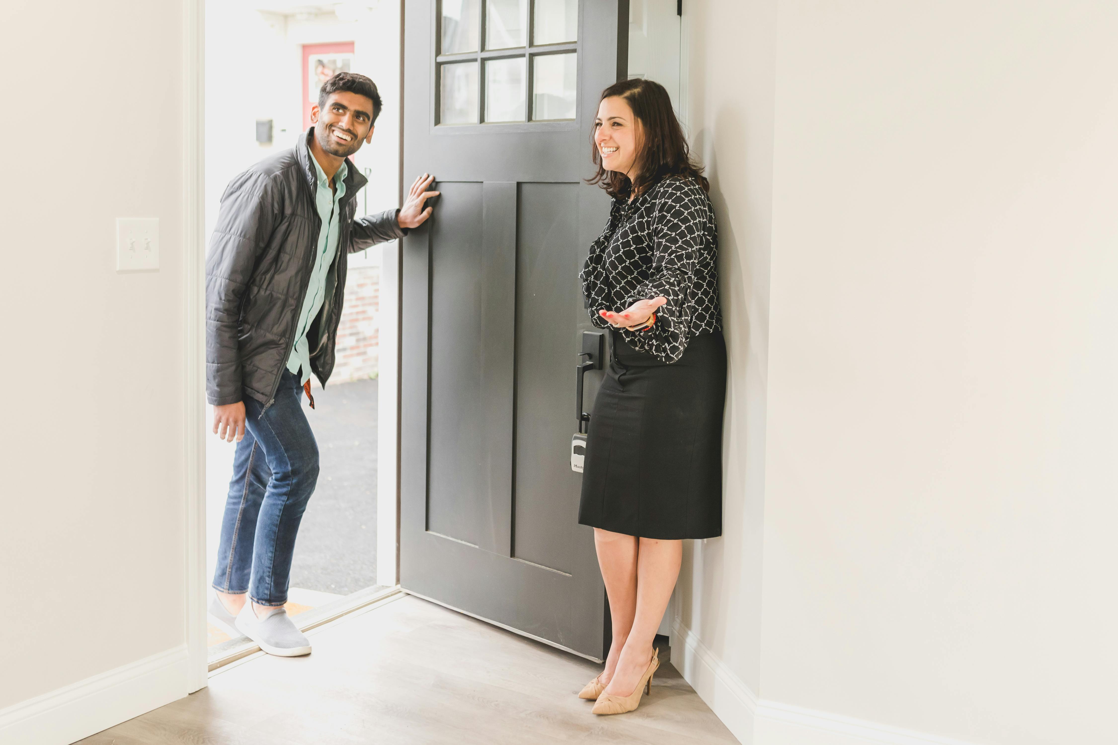 Real estate agent welcoming visitors at an open house, standing in a well-staged living room while pointing out features of the home.