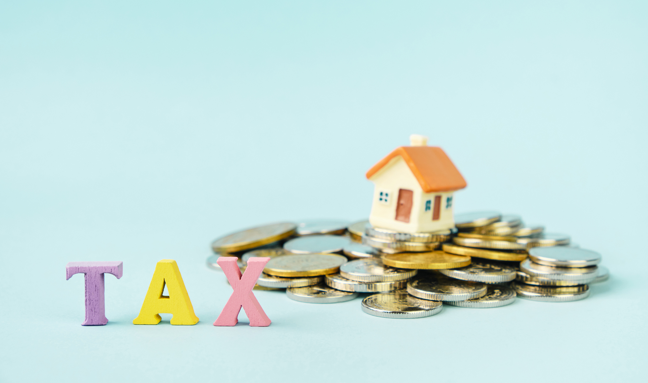 Photo of a small model house on top of a pile of change with the word TAX in toy letters in front of it.