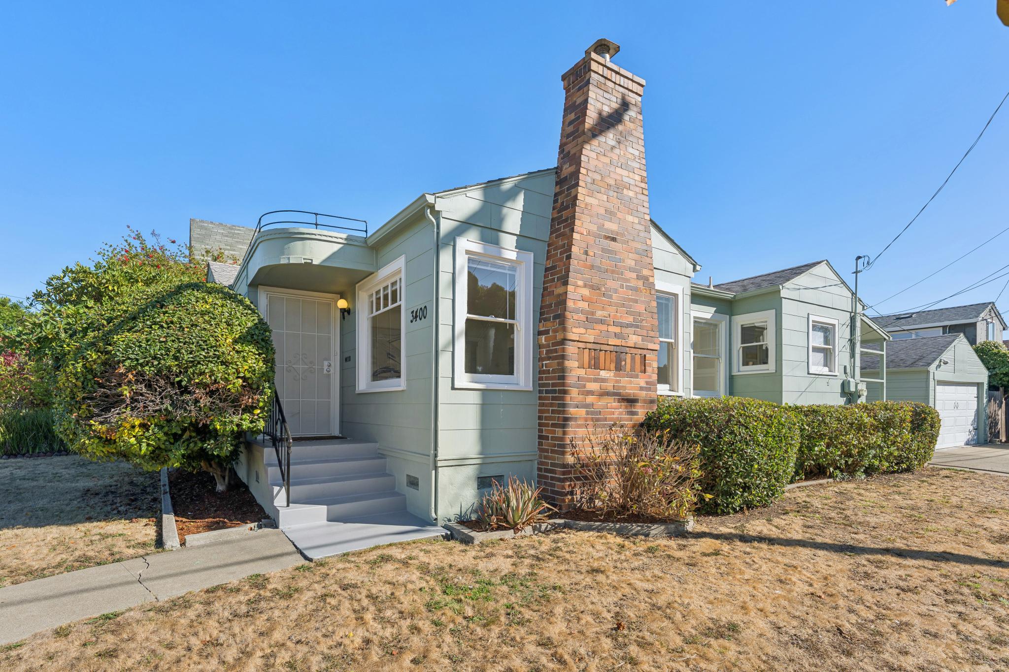 Front exterior of 3400 McBryde Ave in North and East, Richmond, featuring pale green siding, a brick chimney, curved entry canopy, and front yard.