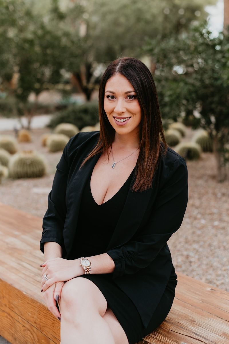 Leah Silva Sitting on a Rock Bench wearing a black dress smiling with a necklace