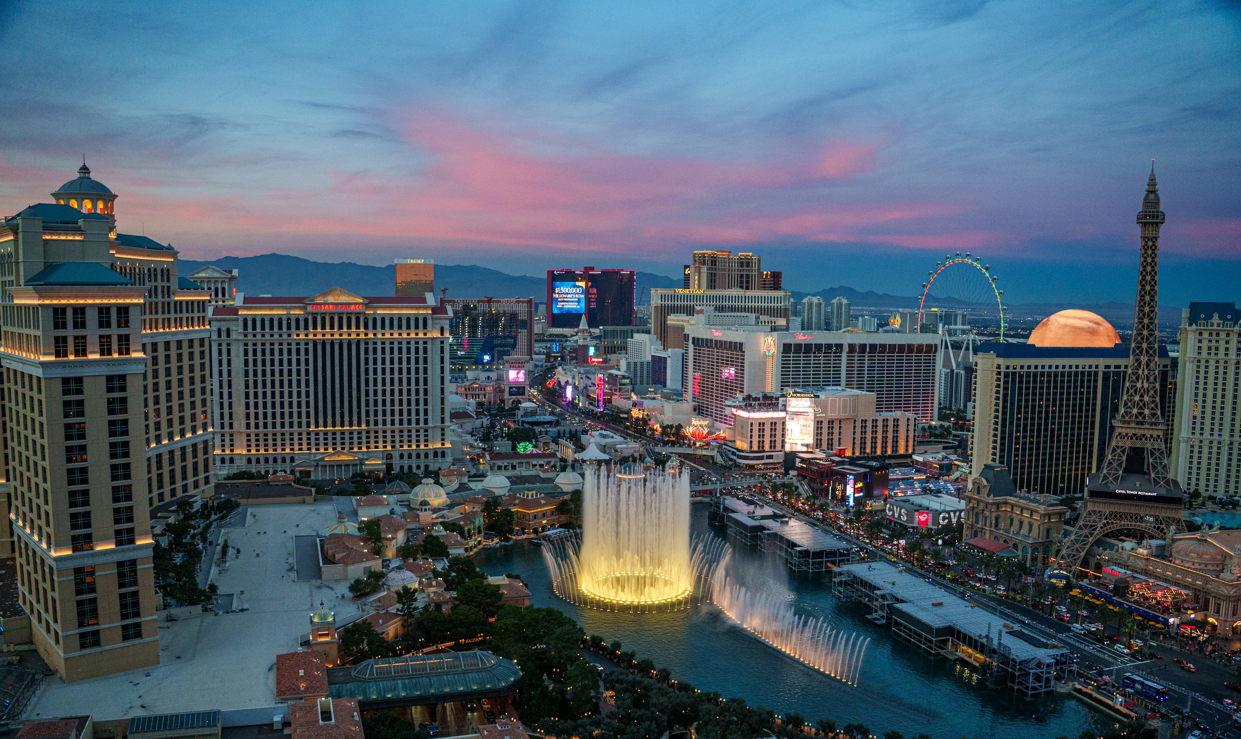 Las Vegas Strip at twilight with Bellagio fountains, Paris Las Vegas Eiffel Tower, and illuminated luxury resorts under a pink and indigo dusk sky