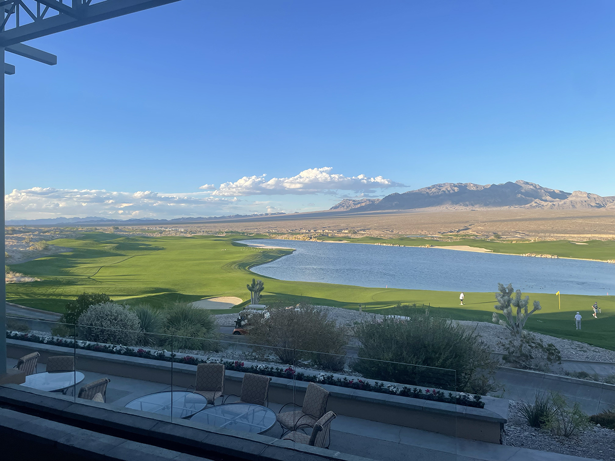 Green desert golf course fairways and a pond with cactus and rugged mountains under a blue sky in Las Vegas.