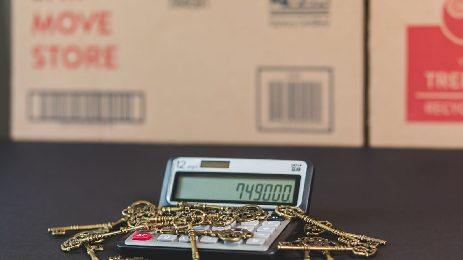 Calculator showing a home value beside house keys and moving boxes
