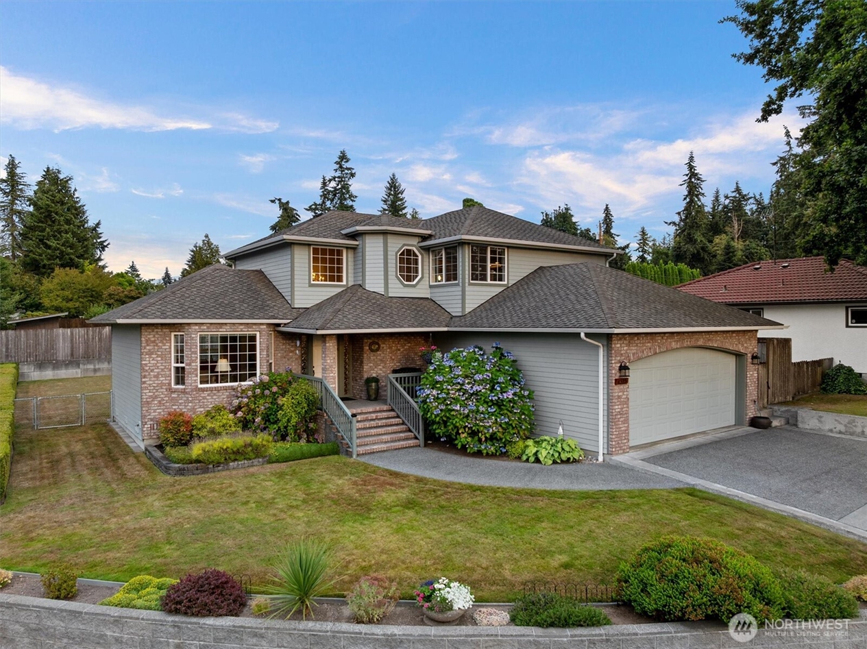 Two-story home with brick exterior, landscaped front yard, covered entry, and attached garage, illustrating residential real estate sales in Western Washington.