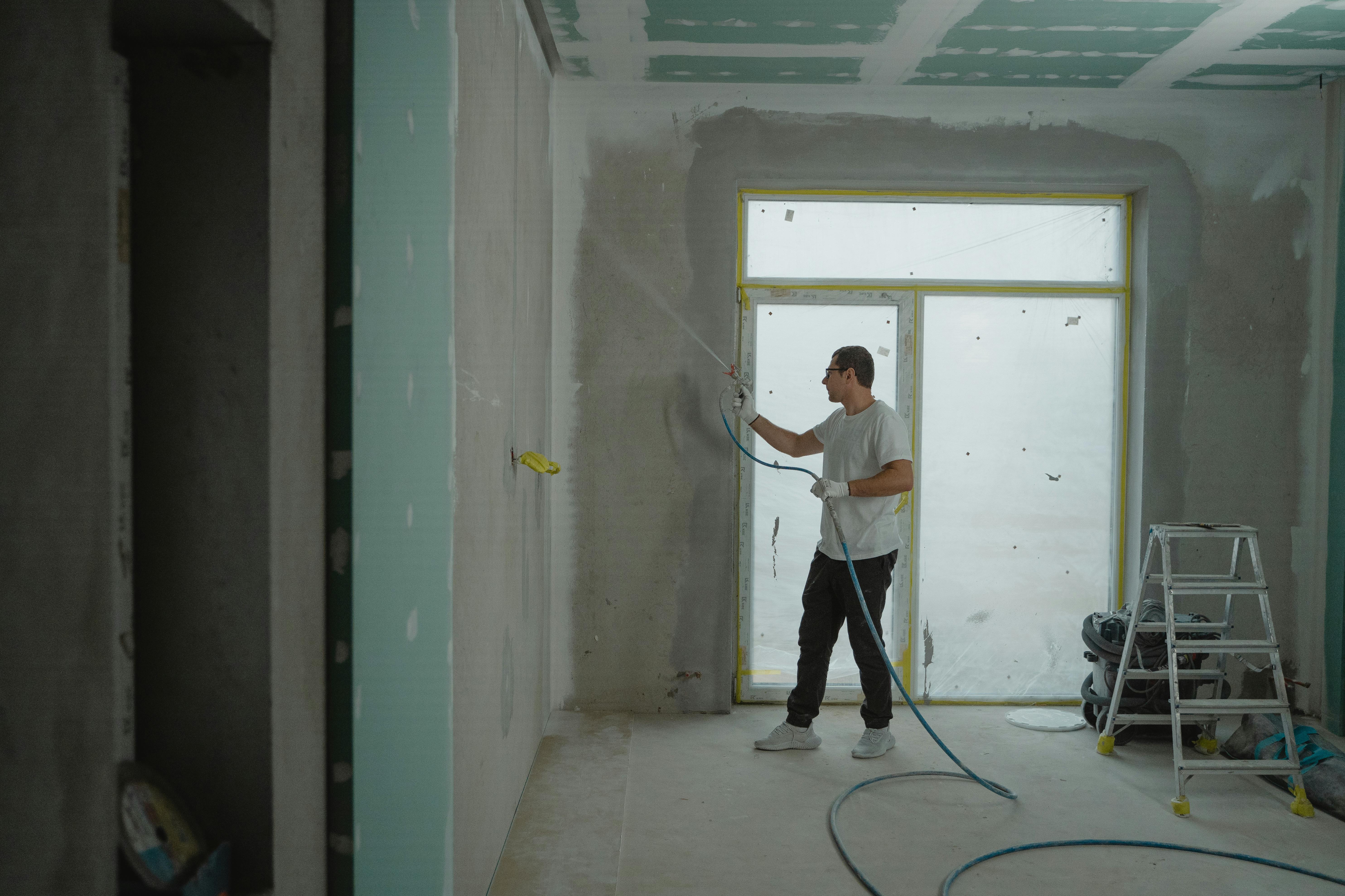 A man spraying paint to remodel a bedroom