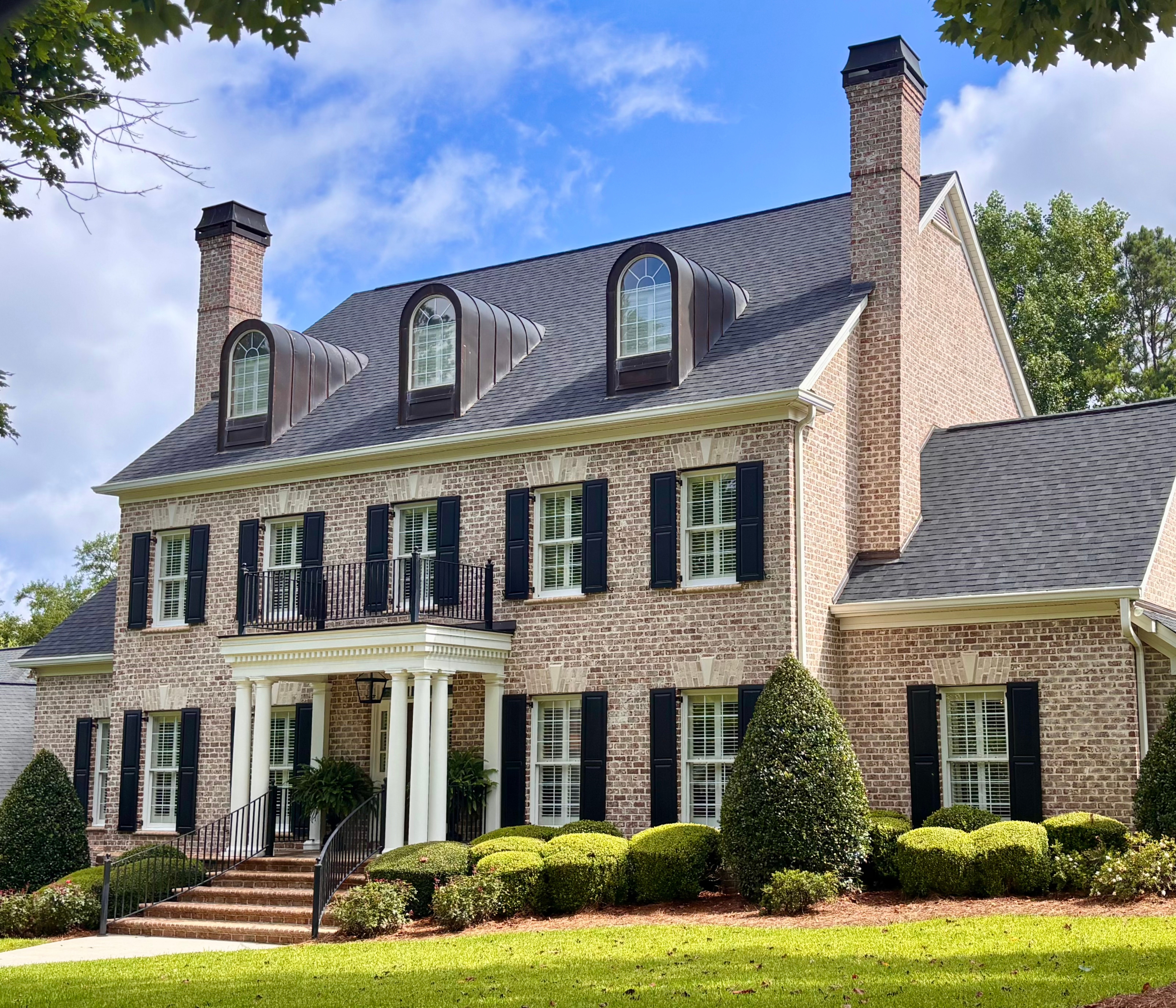 Traditional brick home in the Providence neighborhood of Macon, GA featuring black shutters, dormer windows, manicured landscaping, and a columned front porch.