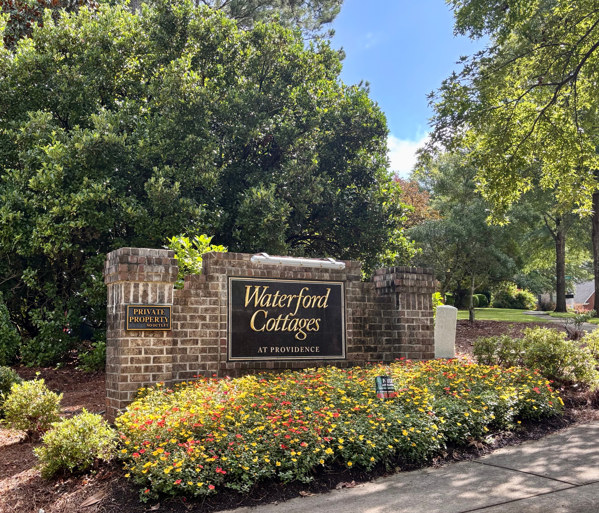 Entrance sign for Waterford Cottages at Providence, a 55+ community in Macon, GA, featuring a brick monument surrounded by colorful landscaping and mature trees.