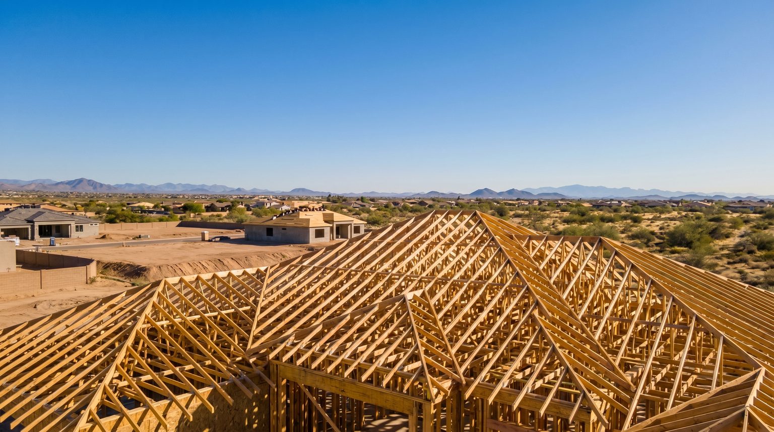 A partially framed roof truss structure against the sky, in a Phoenix metro new-construction community, clear blue sky