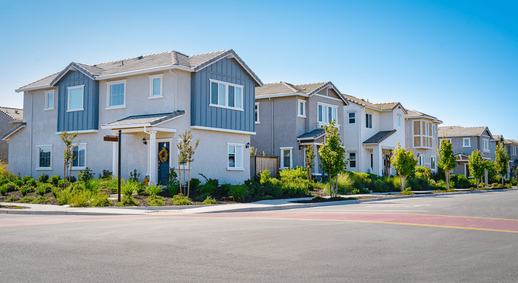 A row of modern, two-story suburban homes with blue and grey siding under a clear blue sky, representing residential real estate options.