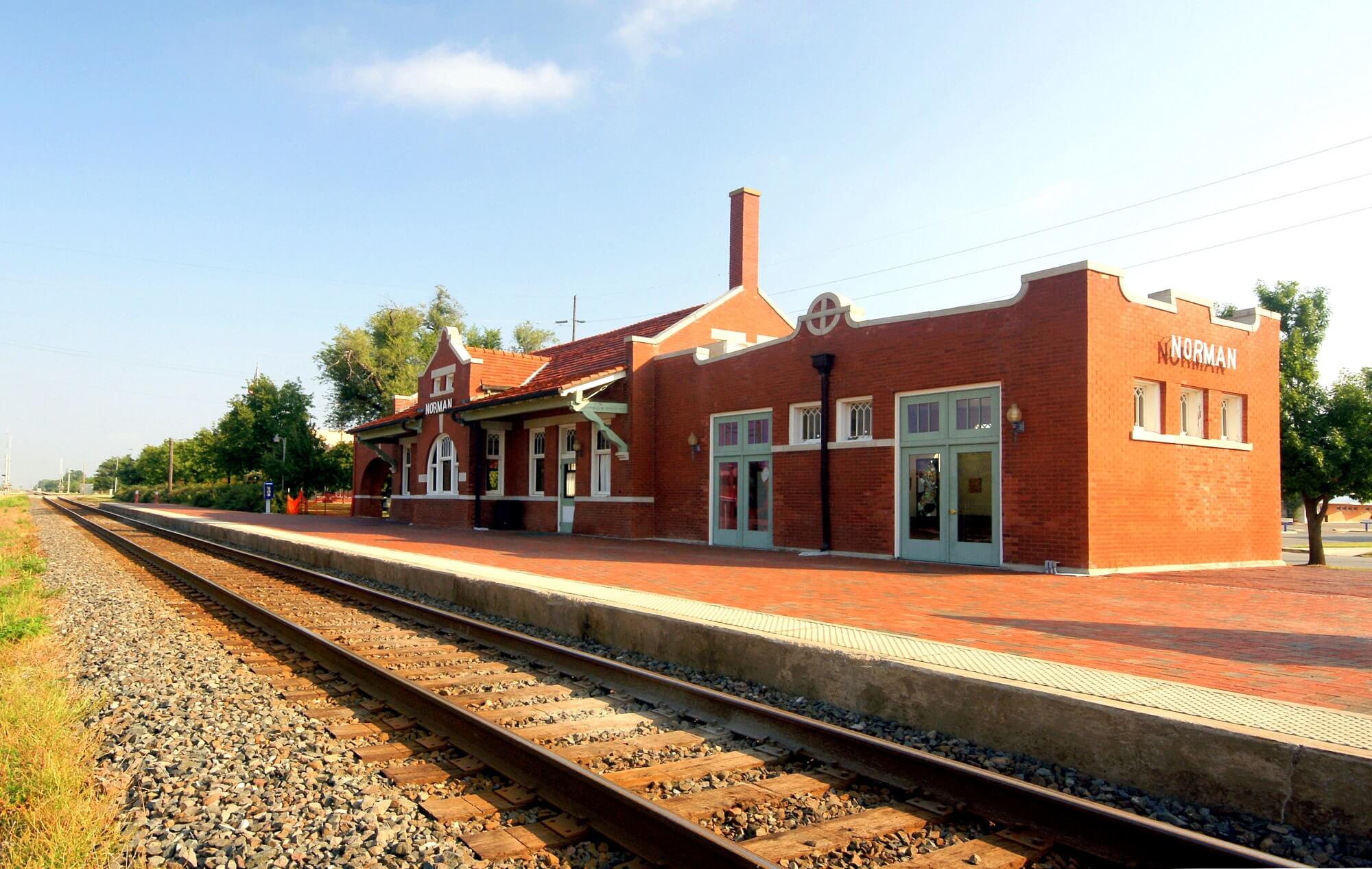 A small-town main street with brick storefronts and a train station in autumn.