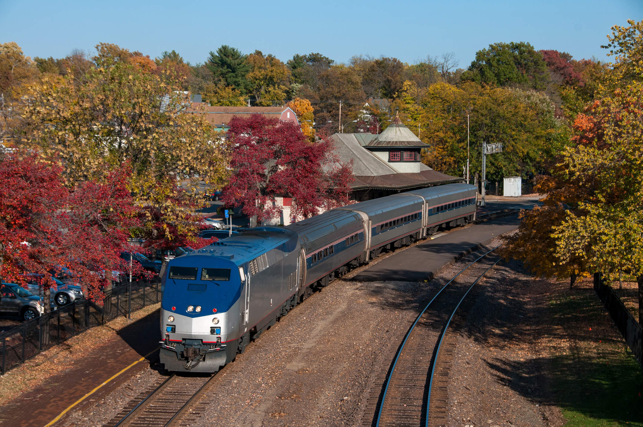 A small-town main street with brick storefronts and a train station in autumn.