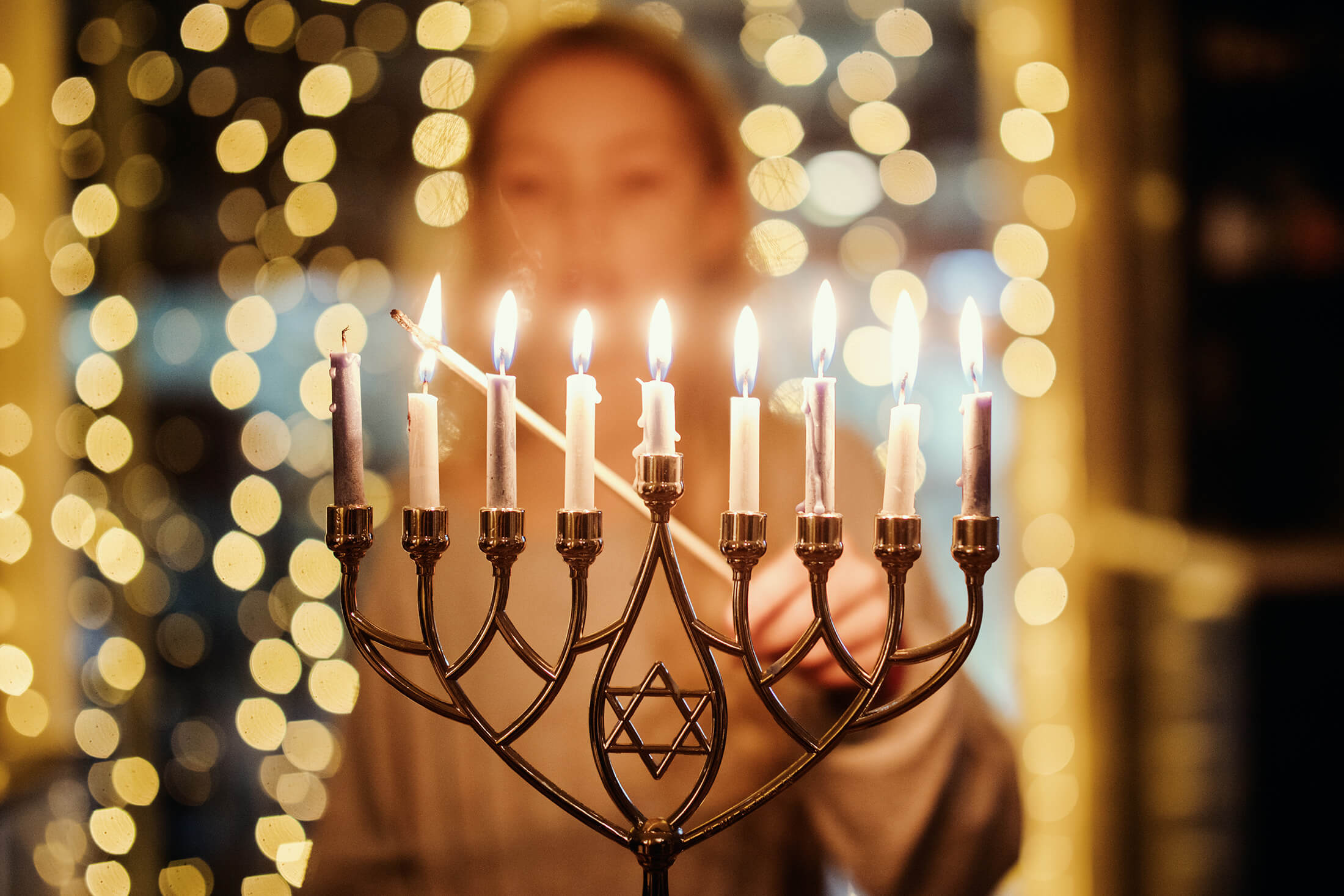 hanukkah-menorah-being-lit-with-bokeh-lights-in-background