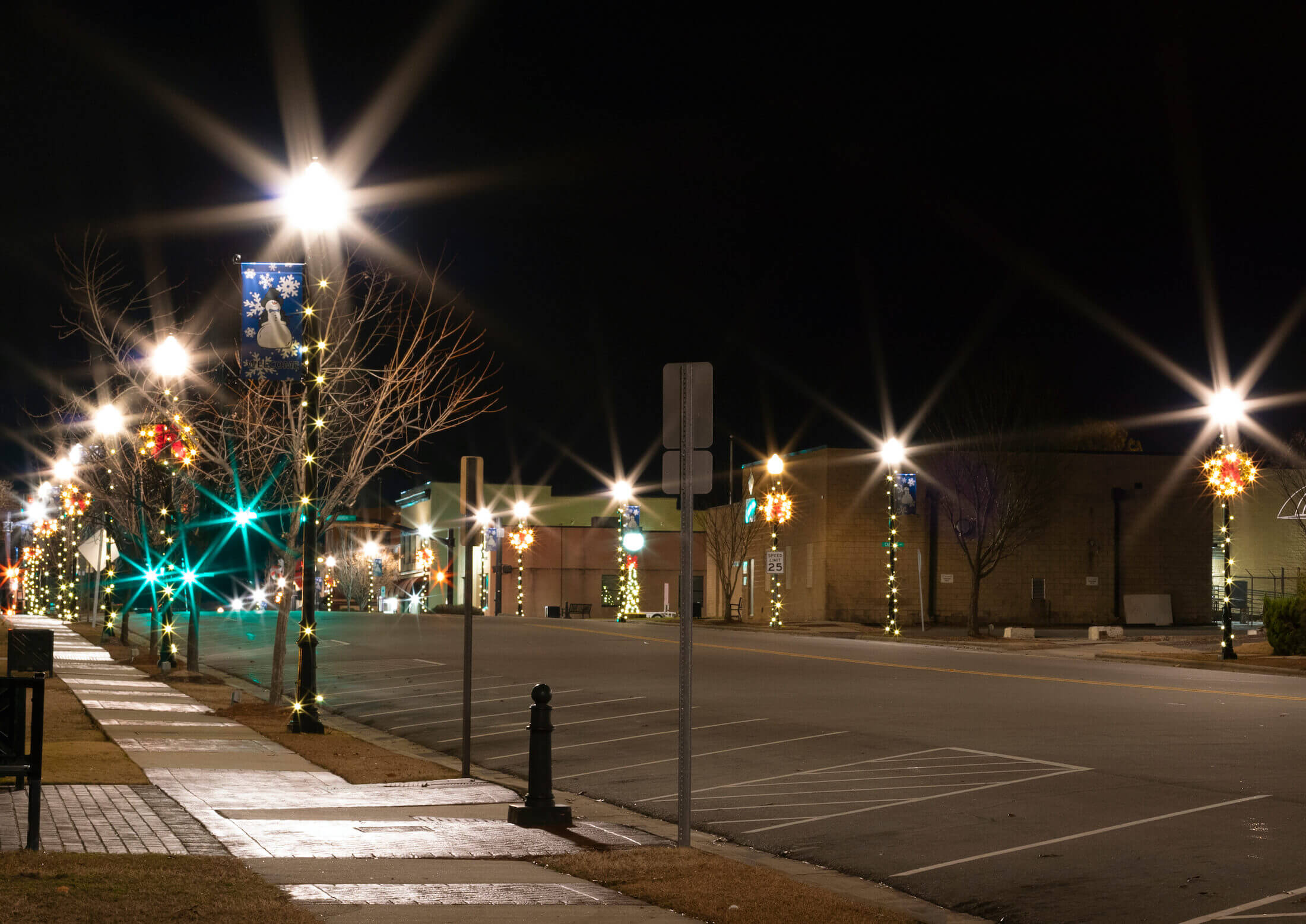 A downtown shopping street at dusk with warm holiday lights and a light dusting of snow.