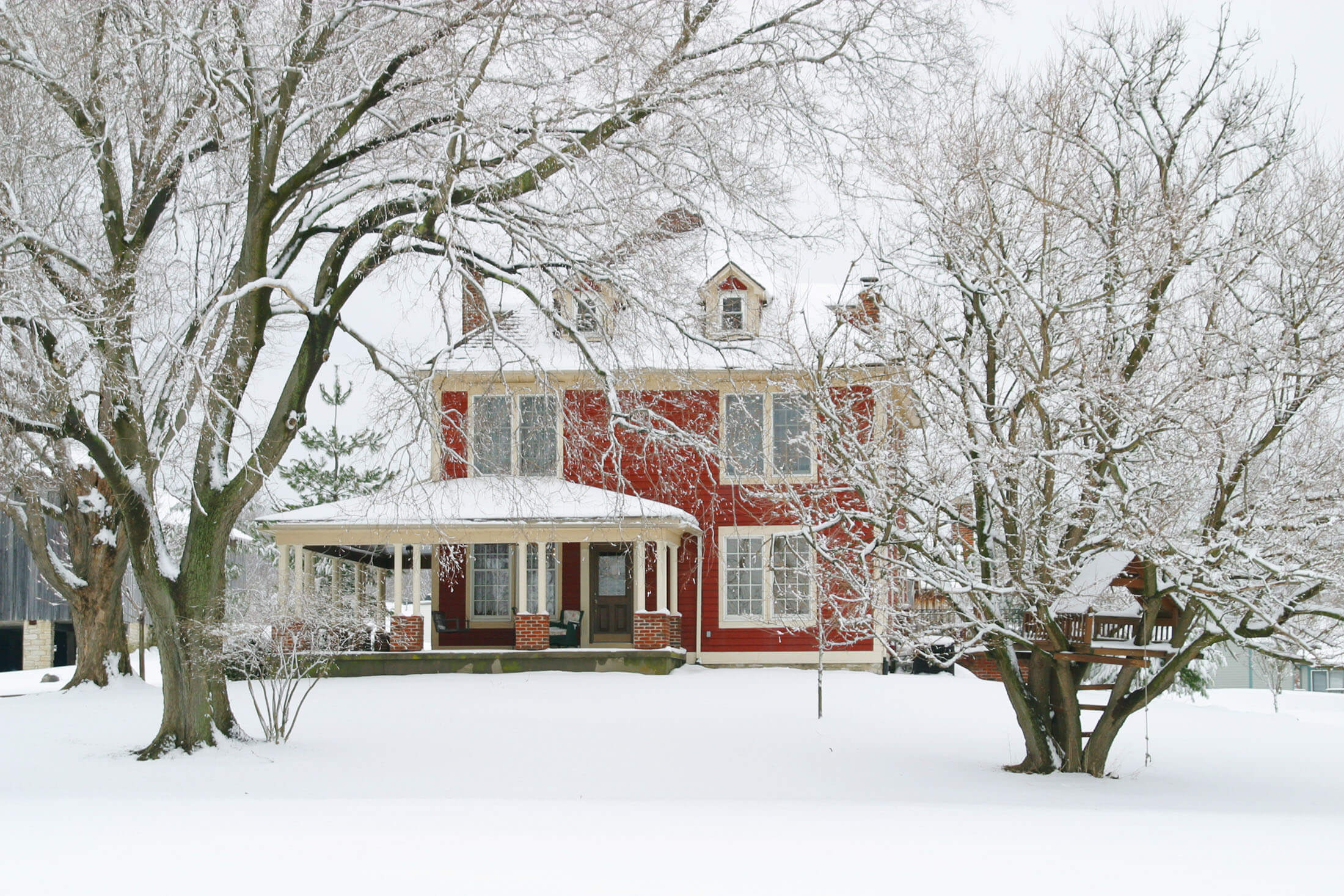 farmhouse-winter-scene-red-exterior-wraparound-porch-snow-covered