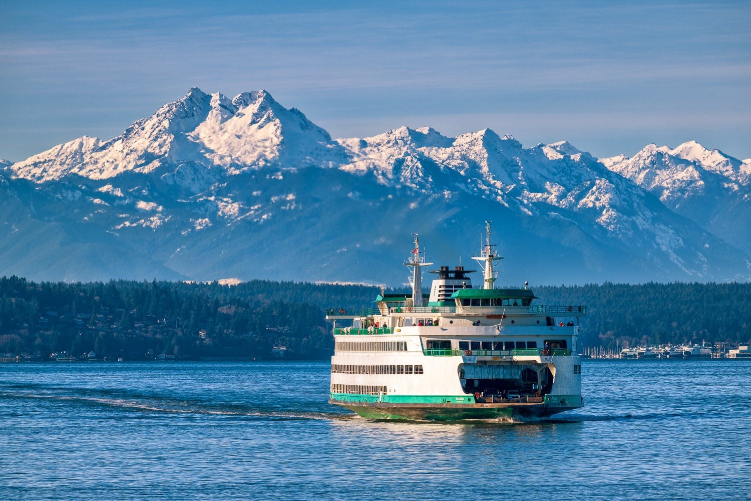 Washington State ferry crossing Puget Sound with the snow-capped Olympic Mountains in the background on a clear day, symbolizing travel from Whidbey Island to Seattle.