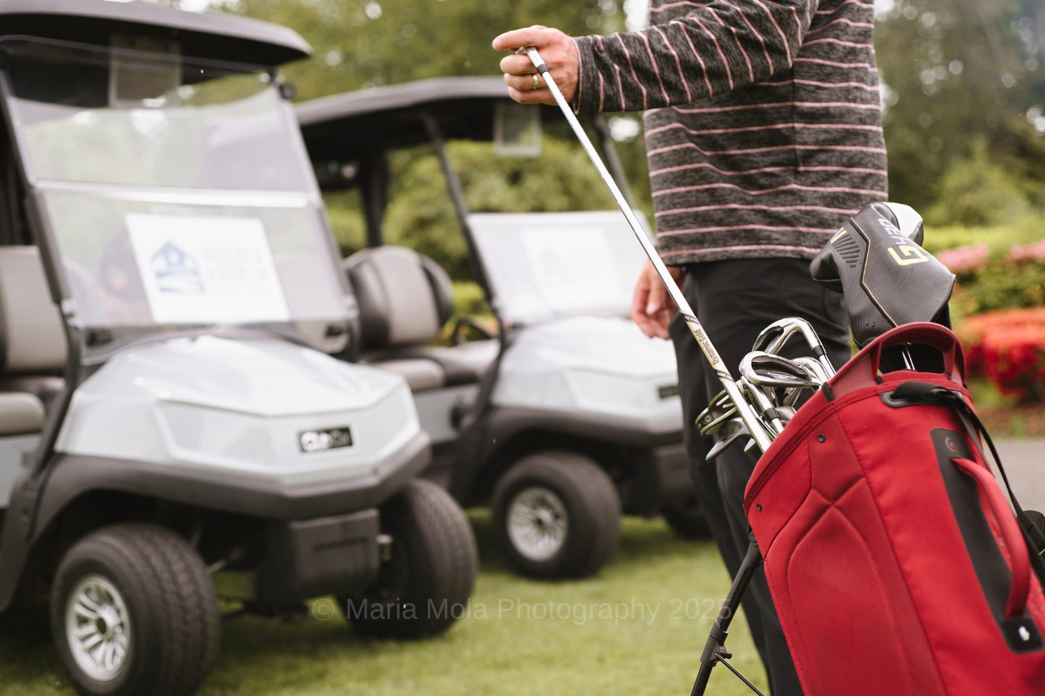 A hand pulling out a golf club from a bag of clubs in front of golf carts.