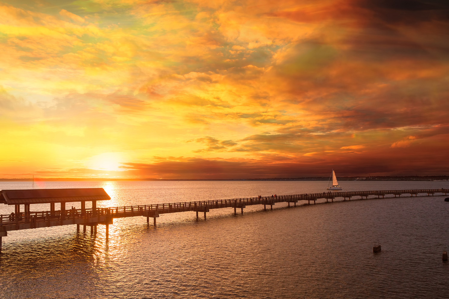A sail boat with a sunset in front of Boulevard Park Pier in Bellingham, WA