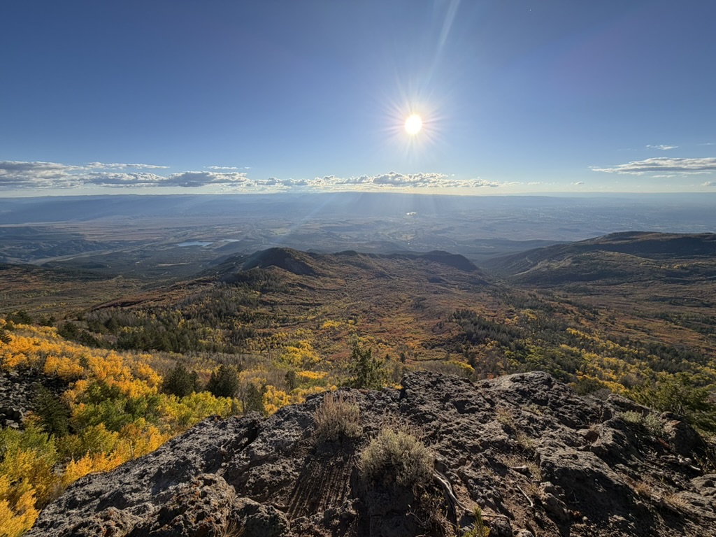 View from the summit of Grand Mesa looking out over golden aspen groves and the Grand Valley below at sunset.