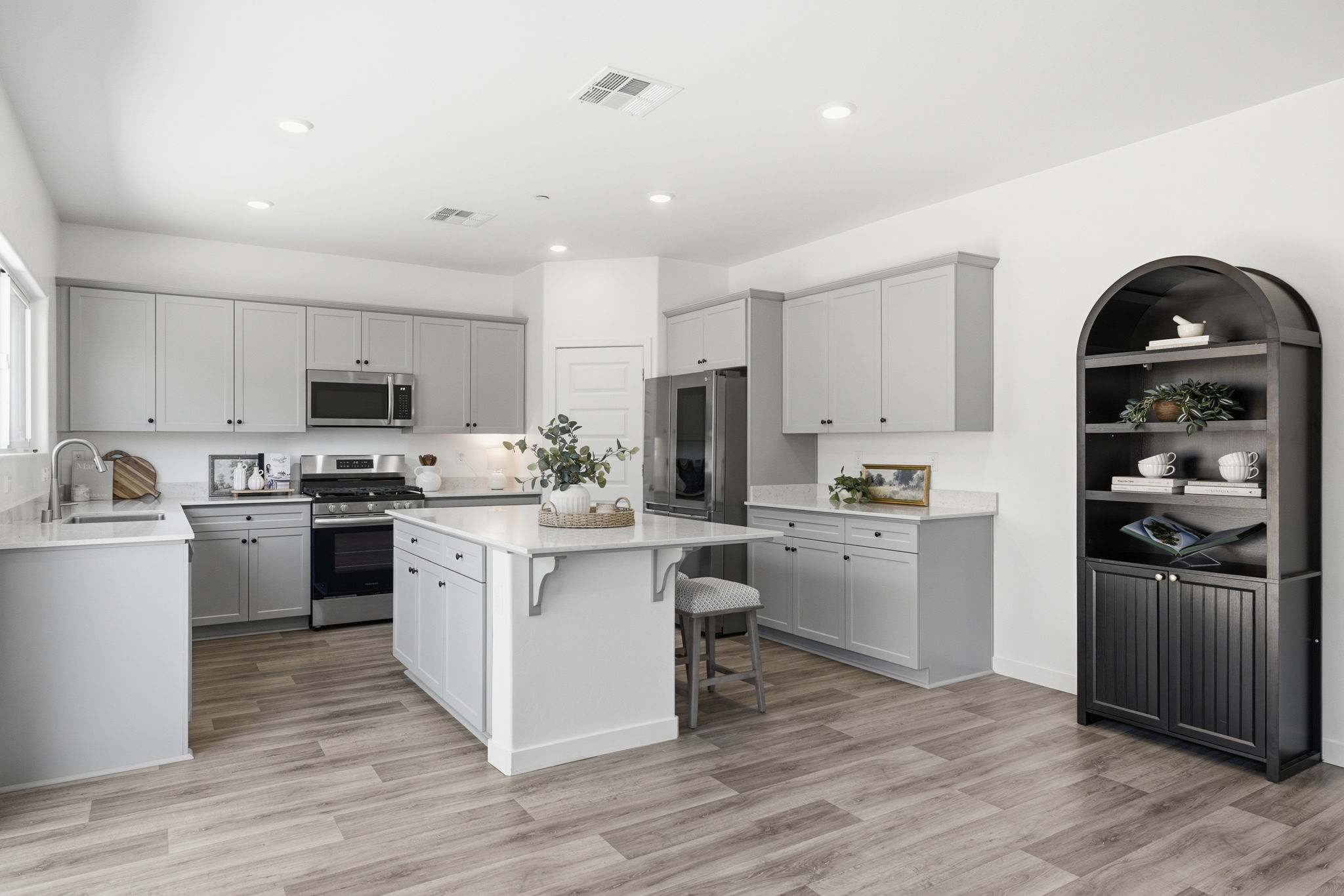 Modern kitchen in a Bakersfield home with large center island, gray cabinets, stainless steel appliances and wood-look flooring.