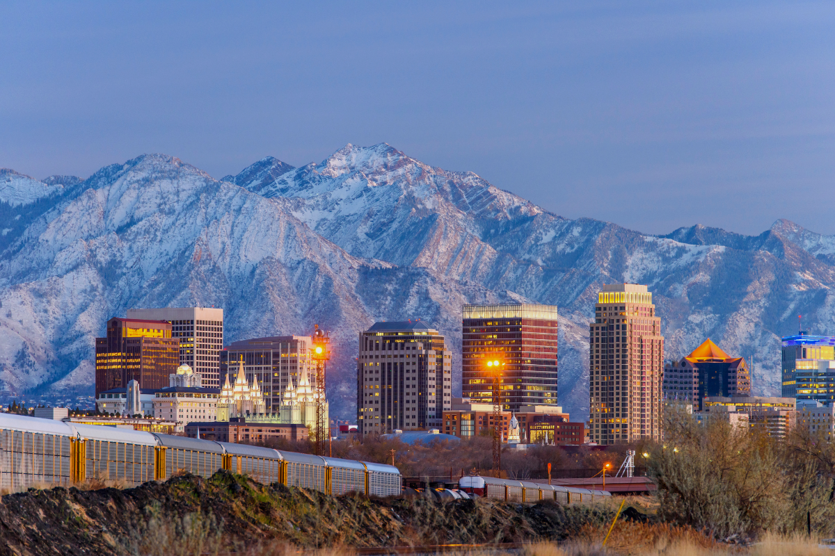 Salt Lake City skyline at dusk with illuminated buildings against the snow-capped Wasatch Mountains, showcasing Utah's urban development in areas affected by new housing type amendments