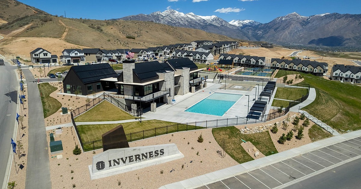 Drone aerial of the existing Inverness community in Lehi, Utah, showing the INVERNESS monument sign, clubhouse, pool and nearby townhomes with the Wasatch Mountains behind.