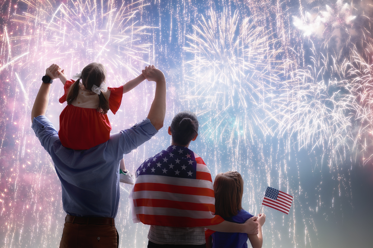 American family celebrating 4th of July watching colorful fireworks display with child on father's shoulders and patriotic clothing