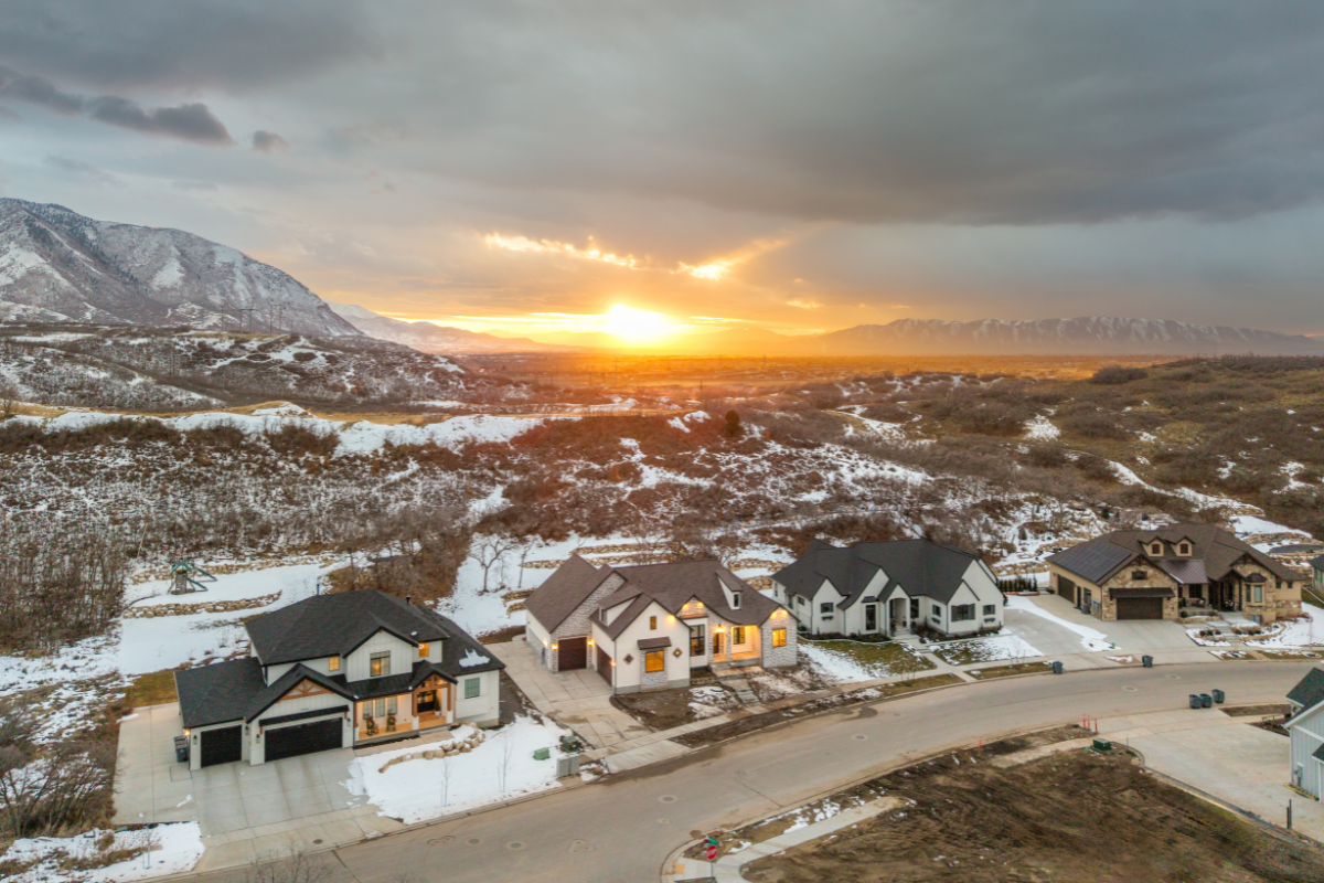 Aerial view of Utah homes in winter with snow-covered hills and a sunset over the mountains, highlighting seasonal curb appeal and scenic neighborhood landscape.