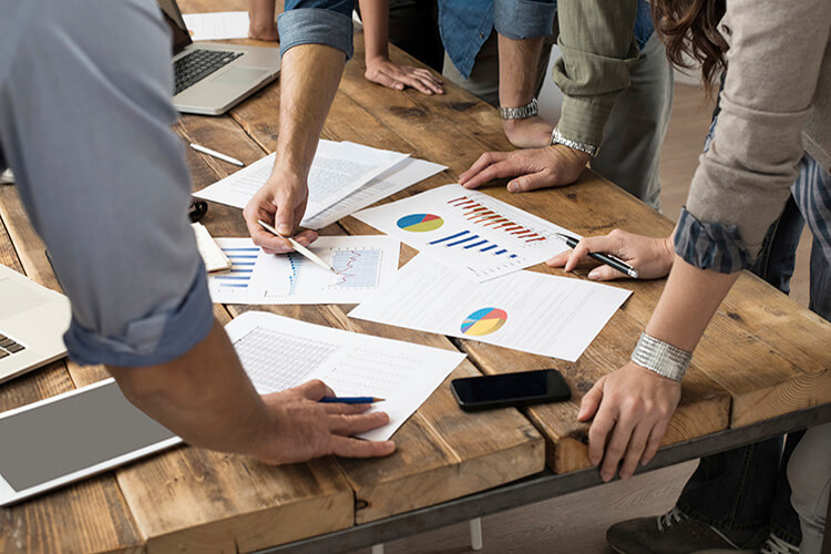 A team of professionals reviewing real estate data and market trends on charts and documents to develop a strategic selling plan