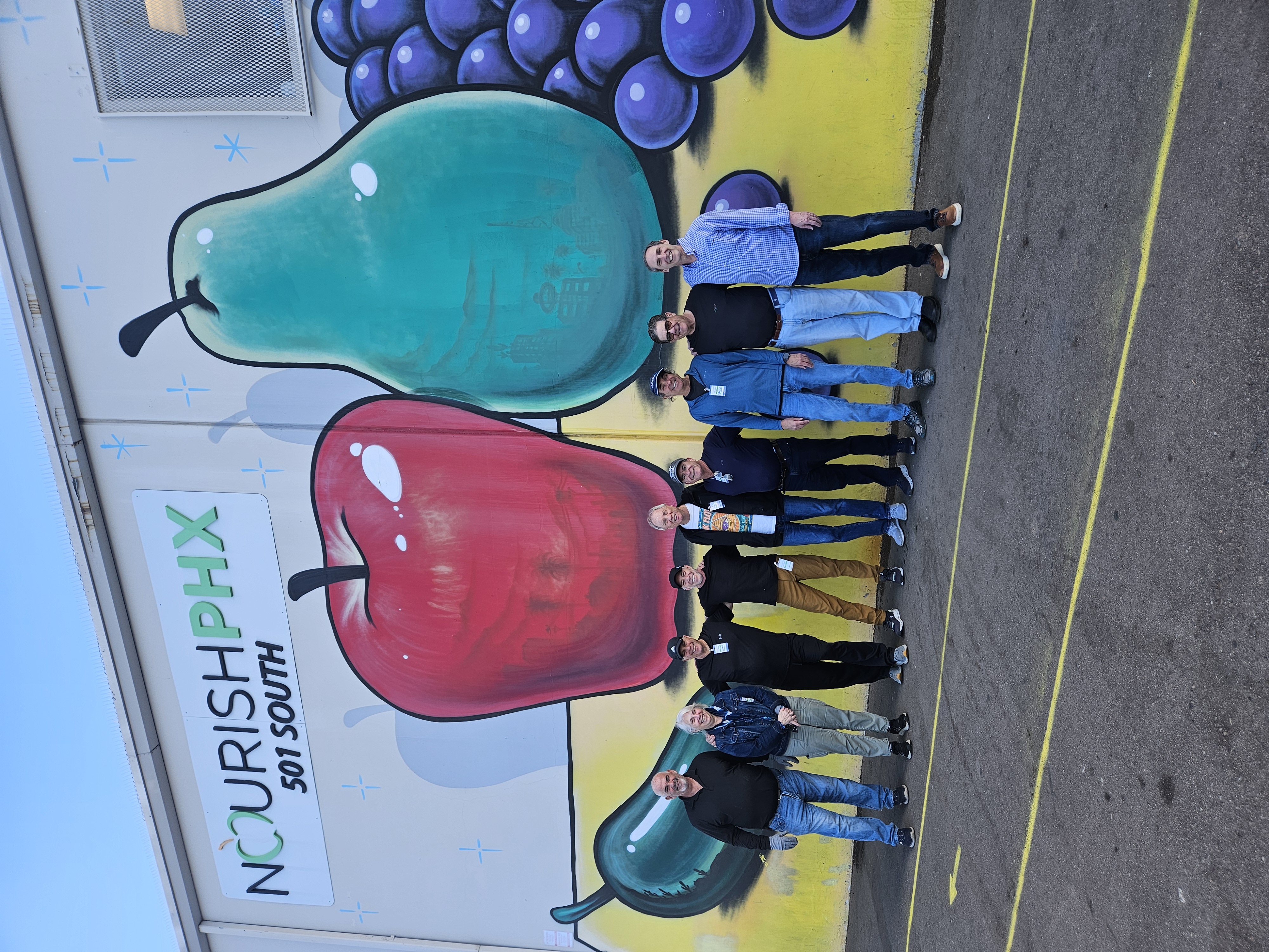 Volunteers at Nourish Phoenix standing in front of colorful fruit sculptures during a community service event with HomeBright Realty.