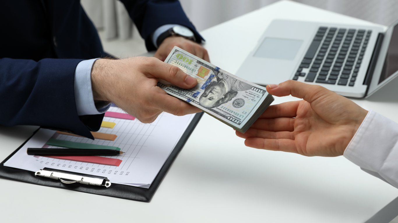 Businessperson handing over a stack of hundred-dollar bills in an office setting, symbolizing real estate financing, investment funding, or property loan approval.