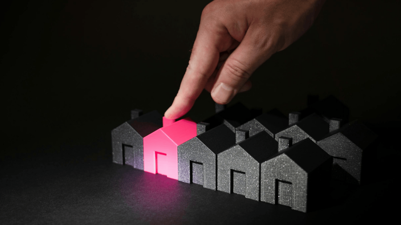 Choosing the right investment property concept — a hand pointing at a highlighted pink house among black houses, symbolizing real estate selection and property investment opportunities in Los Angeles.